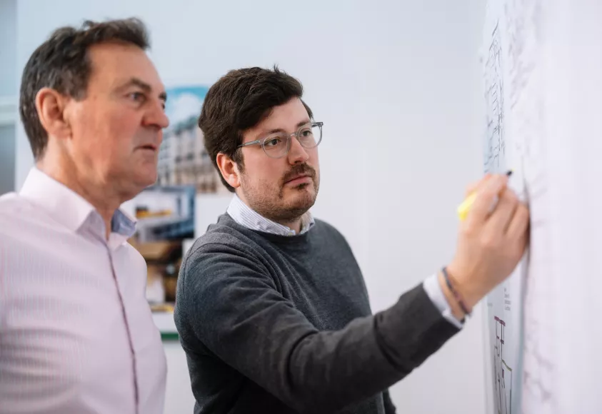 Geschäftsführer Maximilian Meierhofer mit Mitarbeiter vor Plan an Wand